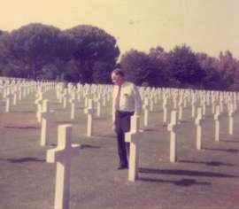Bill Prince standing in cemetery in Nettuno, Italy among grave markers.